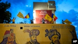 دائیں بازو کی پارٹی الائنس فار دی یونیفیکیشن آف رومانین (AUR) کے حامی جھنڈے لہراتے ہوئے ایک بڑے پوسٹر کے اوپر کھڑے ہیں جس میں قرون وسطی کےحکمرانوں کو دکھایا گیا ہے۔ (اے پی فوٹو)