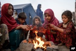 طورخم بارڈر پر ایک پناہ گزین کیمپ میں پاکستان سےافغٓانستان واپس جانے والے کچھ افغان بچے سردی سے بچنے کی کوشش میں ، فوٹو اے پی 4 نومبر 2023