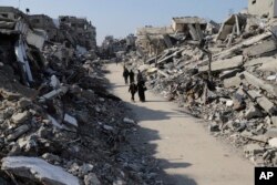 کچھ فلسطینی غزہ کی پٹی میں قائم جبالیا پناہ گزین کیمپ سے گزر رہے ہیں۔ اردگرد اسرائیلی بمباری میں تباہ ہونے والے مکانوں کے ملبوں کے ڈھیر پڑے ہیں۔29 فروری 2024