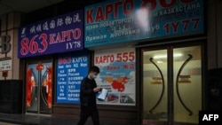 بیجنگ کی ایک سڑک پر ایک شخص 'شپنگ کارگو' کے اشتہار والی ایک عمارت کے سامنے سے گزر رہا ہے۔ 4 مارچ، 2022ء 