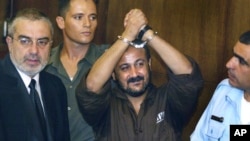  مروان برغوتی، 14 اگست 2002 کو تل ابیب کی ایک عدالت میں اپنے مقدمے کی سماعت کے پہلے دن اپنے ہتھکڑی والے ہاتھ ہوا میں اٹھا رہے ہیں۔ (اے پی فوٹو)
