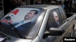 Hình ảnh Tổng thống Syria Bashar al-Assad và Tổng thống Nga Vladimir Putin trên kính một chiếc xe gần thị trấn Latakia, Syria.