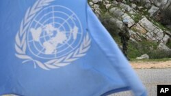 Một binh sĩ gìn giữ hòa bình đứng phía sau lá cờ Liên Hiệp Quốc.